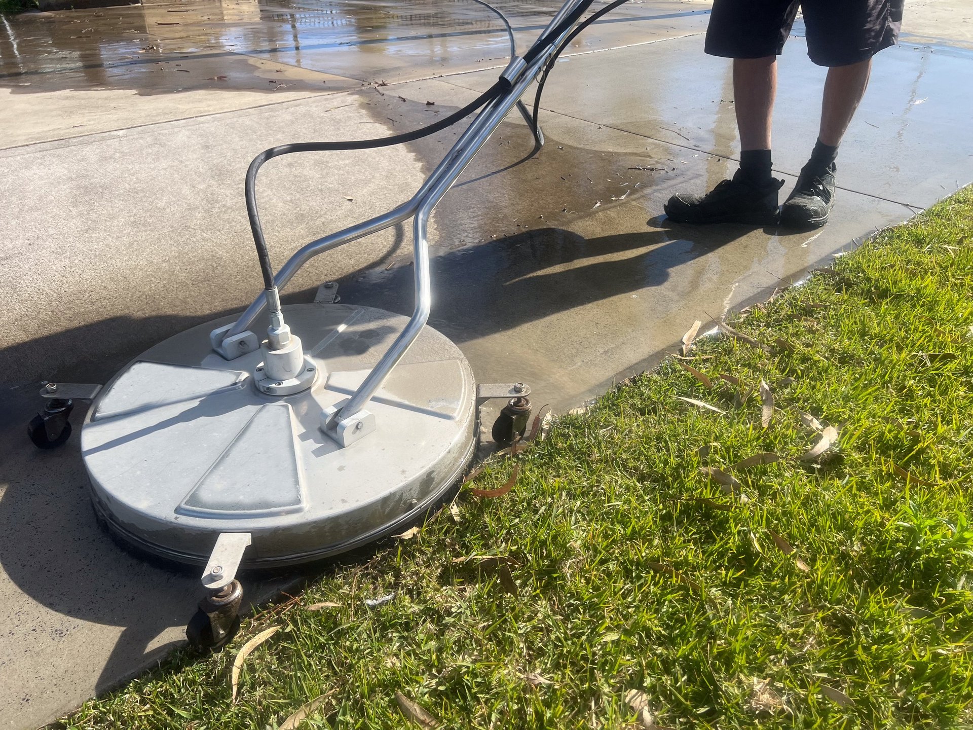 Worker using a floor and surface pressure washer cleaner high-pressure water spray to remove loose paint, mold, grime, dust, mud, and dirt from surfaces and objects.